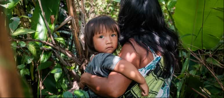 Mujer indígena ka'apor entre la vegetación de la selva amazónica con su hijo en brazos