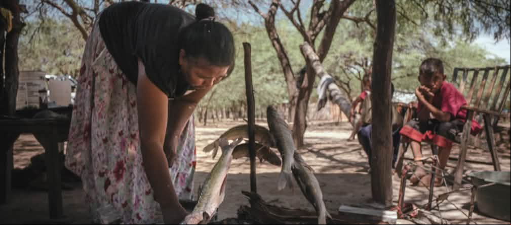 Mujer asando pescado bajo la atenta mirada de dos niños